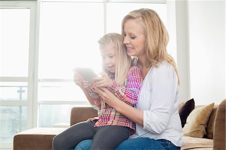 Happy woman with daughter using digital tablet in living room Stock Photo - Premium Royalty-Free, Code: 693-07542232