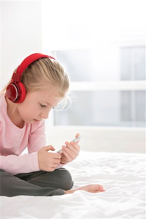 Cute girl listening music on smart phone in bedroom Stock Photo - Premium Royalty-Free, Code: 693-07542253