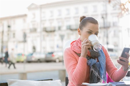 pictures of winter in europe - Young woman drinking coffee while using cell phone at sidewalk cafe Stock Photo - Premium Royalty-Free, Code: 693-07542272