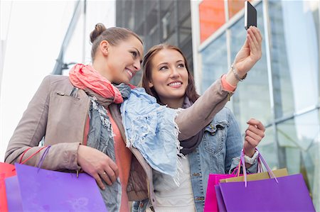 Female friends with shopping bags taking self portrait through mobile phone Fotografie stock - Premium Royalty-Free, Codice: 693-07542305