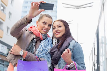 Female friends with shopping bags taking photos through mobile phone Fotografie stock - Premium Royalty-Free, Codice: 693-07542306