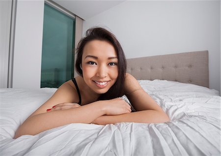 Portrait of happy young woman resting in bed Stock Photo - Premium Royalty-Free, Code: 693-07542347