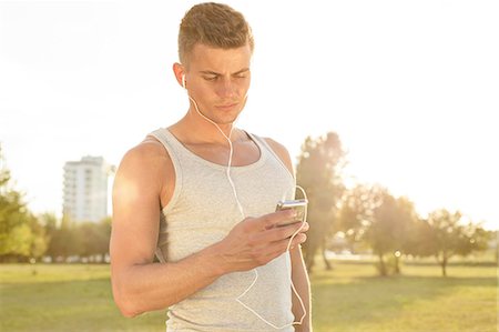 Young jogger listening to music through cell phone in park Stock Photo - Premium Royalty-Free, Code: 693-07672613