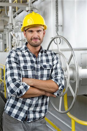 Portrait of worker with arms crossed leaning on large valve in industry Photographie de stock - Premium Libres de Droits, Code: 693-07672631