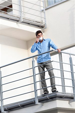 Full length of young businessman drinking coffee at hotel balcony Stock Photo - Premium Royalty-Free, Code: 693-07672654