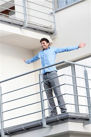 simsearch:693-07672655,k - Full length of smiling young businessman standing arms outstretched at hotel balcony Stock Photo - Premium Royalty-Free, Code: 693-07672652