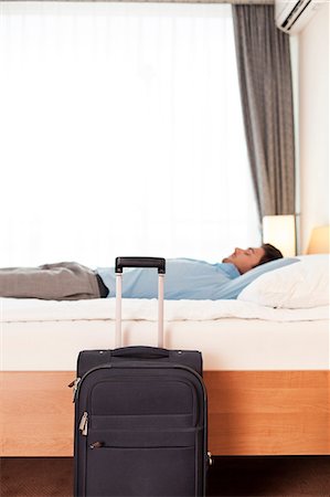 Side view of young businessman sleeping in bed by luggage at hotel Stock Photo - Premium Royalty-Free, Code: 693-07672665