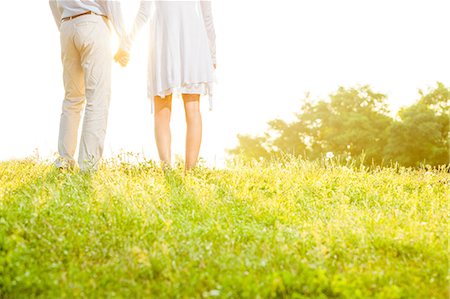 Midsection rear view of couple holding hands while standing on grass against sky Stock Photo - Premium Royalty-Free, Code: 693-07672752
