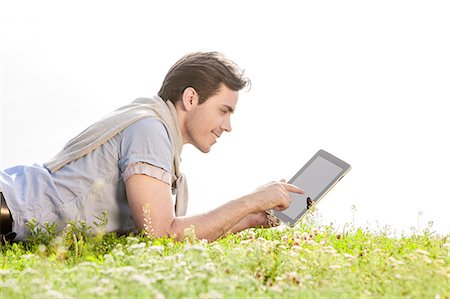 simsearch:693-07673302,k - Side view of young man using digital tablet while lying on grass against clear sky Photographie de stock - Premium Libres de Droits, Code: 693-07672784