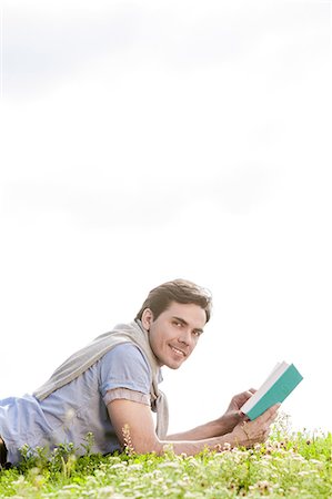 simsearch:693-07672803,k - Side view portrait of young man holding book while lying on grass against clear sky Stock Photo - Premium Royalty-Free, Code: 693-07672787