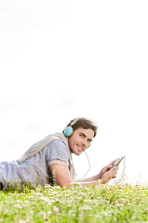 simsearch:693-07672615,k - Side view portrait of man listening to music on MP3 player using headphones in park against clear sky Fotografie stock - Premium Royalty-Free, Codice: 693-07672789