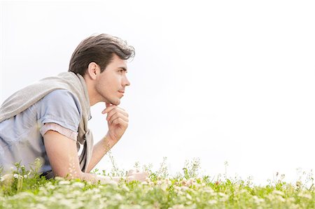 simsearch:693-07672803,k - Side view of thoughtful young man lying on grass against clear sky Stock Photo - Premium Royalty-Free, Code: 693-07672780