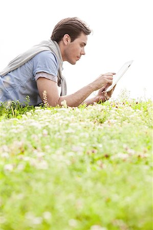simsearch:693-07673302,k - Side view of young man using digital tablet while lying on grass against clear sky Stock Photo - Premium Royalty-Free, Code: 693-07672783