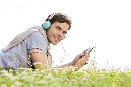 simsearch:693-07672803,k - Side view portrait of man listening to music on MP3 player using headphones in park against clear sky Stock Photo - Premium Royalty-Free, Code: 693-07672790