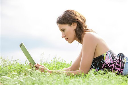 simsearch:693-07542215,k - Side view of young woman using Tablet PC while lying on grass against sky Foto de stock - Sin royalties Premium, Código: 693-07672802