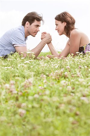 Profile shot of couple arm wrestling while lying on grass against sky Stock Photo - Premium Royalty-Free, Code: 693-07672813