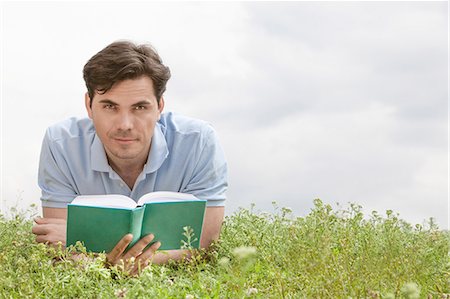 simsearch:693-07672803,k - Portrait of young man holding book while lying on grass against sky Stock Photo - Premium Royalty-Free, Code: 693-07672821