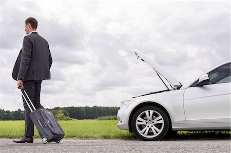 Full length rear view of young businessman with luggage leaving broken down car at countryside Stock Photo - Premium Royalty-Free, Code: 693-07672839