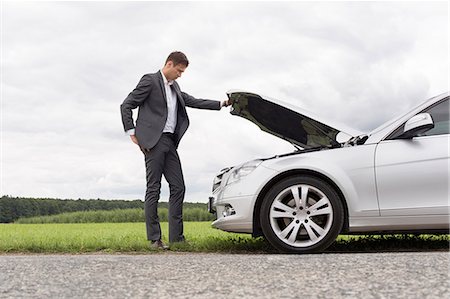 damaged - Full length side view of young businessman examining broken down car engine at countryside Stock Photo - Premium Royalty-Free, Code: 693-07672831