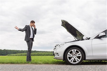 Frustrated young businessman using cell phone by broken-down car at countryside Foto de stock - Sin royalties Premium, Código: 693-07672832