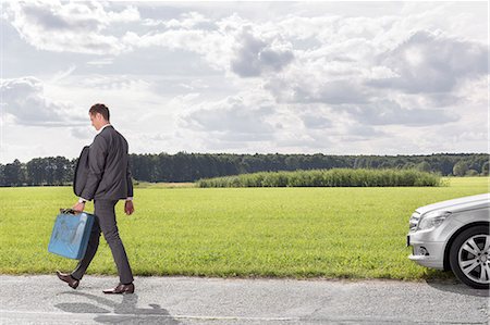 Full length of young businessman with gas can leaving broken down car at countryside Stock Photo - Premium Royalty-Free, Code: 693-07672851