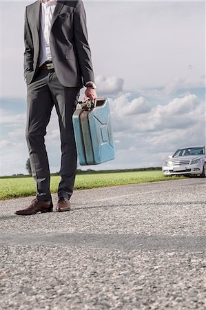 defeat - Low section of young businessman carrying petrol can with broken car in background at countryside Stock Photo - Premium Royalty-Free, Code: 693-07672852