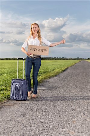 Full length of woman hitching while holding anywhere sign on countryside Stock Photo - Premium Royalty-Free, Code: 693-07672861