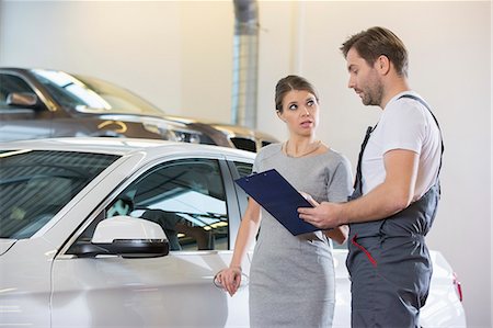 Repairman holding clipboard while conversing with female customer in automobile repair shop Foto de stock - Sin royalties Premium, Código: 693-07672932