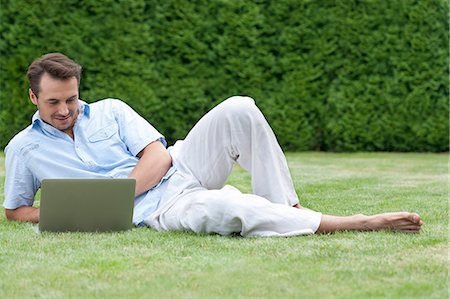 simsearch:693-07672803,k - Full length of young man using laptop while lying on grass in park Stock Photo - Premium Royalty-Free, Code: 693-07673048