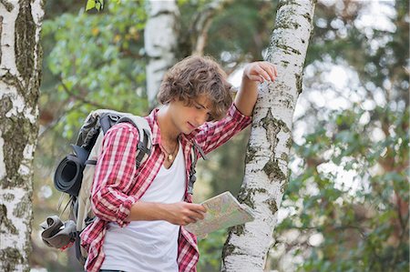 Backpacker reading map while leaning on tree trunk in forest Stock Photo - Premium Royalty-Free, Code: 693-07673174