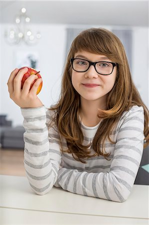 simsearch:693-07542115,k - Portrait of teenage girl holding apple while sitting at table in house Stock Photo - Premium Royalty-Free, Code: 693-07673216
