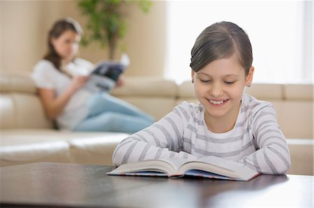 simsearch:693-03363809,k - Smiling girl reading book with mother in background at home Stock Photo - Premium Royalty-Free, Code: 693-07673280