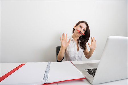 simsearch:693-07672547,k - Astonished businesswoman looking at laptop while holding pen under nose in office Foto de stock - Royalty Free Premium, Número: 693-07912115