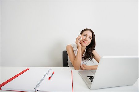 simsearch:693-07455962,k - Smiling businesswoman looking away while answering cell phone at desk in office Stock Photo - Premium Royalty-Free, Code: 693-07912110