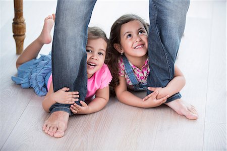 simsearch:6102-05603688,k - Playful girls holding father's legs on hardwood floor Stock Photo - Premium Royalty-Free, Code: 693-07912138