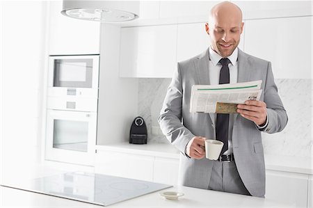 simsearch:693-07456337,k - Mid adult businessman having coffee while reading newspaper in kitchen Photographie de stock - Premium Libres de Droits, Code: 693-07912338