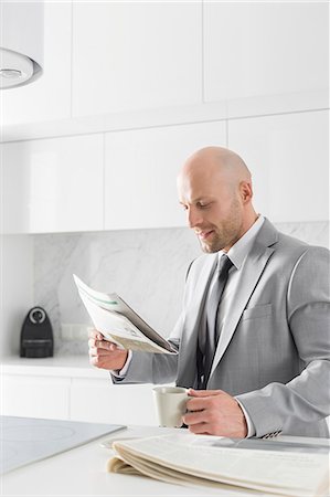 Mid adult businessman having coffee while reading newspaper in kitchen Fotografie stock - Premium Royalty-Free, Codice: 693-07912340