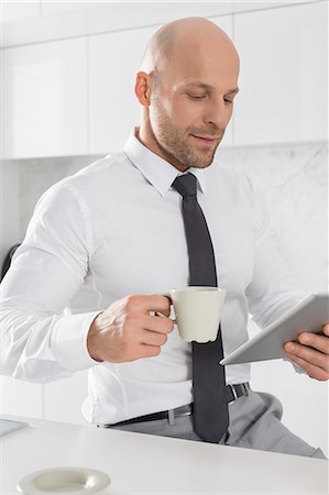 Mid adult businessman having coffee while using tablet PC in kitchen Photographie de stock - Premium Libres de Droits, Code: 693-07912341
