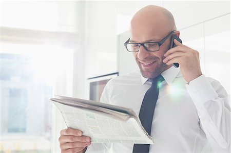 Happy businessman on call while reading newspaper at home Stock Photo - Premium Royalty-Free, Code: 693-07912355