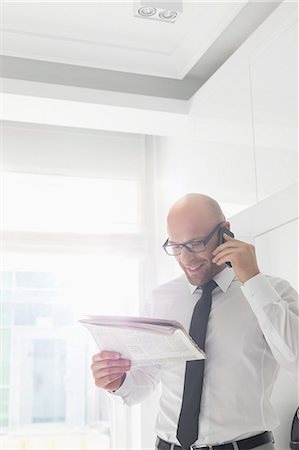 Happy businessman on call while reading newspaper at home Fotografie stock - Premium Royalty-Free, Codice: 693-07912356