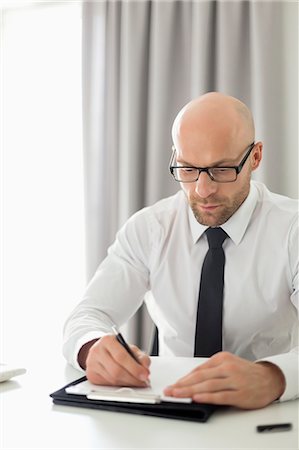 Mid adult businessman writing on clipboard in home office Stock Photo - Premium Royalty-Free, Code: 693-07912364