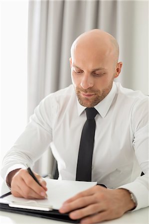 Mid adult businessman writing on clipboard in home office Stock Photo - Premium Royalty-Free, Code: 693-07912365