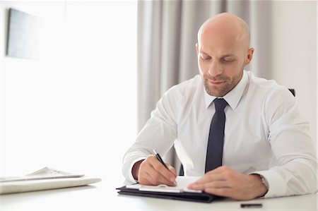 simsearch:693-06379752,k - Mid adult businessman writing on clipboard in home office Photographie de stock - Premium Libres de Droits, Code: 693-07912366