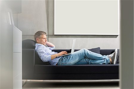 simsearch:693-07542215,k - Full-length side view of Middle-aged man using laptop while lying on sofa Foto de stock - Sin royalties Premium, Código: 693-07912395