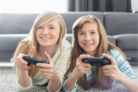 siblings lying - Sisters playing video games in living room Stock Photo - Premium Royalty-Free, Code: 693-07912409