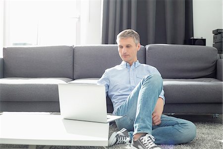 Full-length of man using laptop in living room Photographie de stock - Premium Libres de Droits, Code: 693-07912401