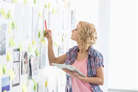 Creative businesswoman analyzing papers stuck on wall in office Stock Photo - Premium Royalty-Free, Code: 693-07912453