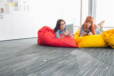 simsearch:614-08119707,k - Businesswomen using digital tablets while relaxing on beanbag chairs in creative office Photographie de stock - Premium Libres de Droits, Code: 693-07912505