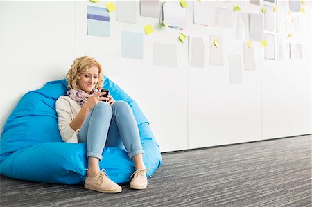 simsearch:693-07912462,k - Smiling businesswoman using mobile phone on beanbag chair in creative office Stock Photo - Premium Royalty-Free, Code: 693-07912506