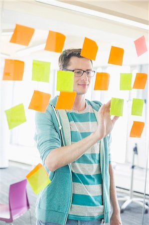 Smiling businessman reading sticky notes on glass wall in creative office Stock Photo - Premium Royalty-Free, Code: 693-07912502